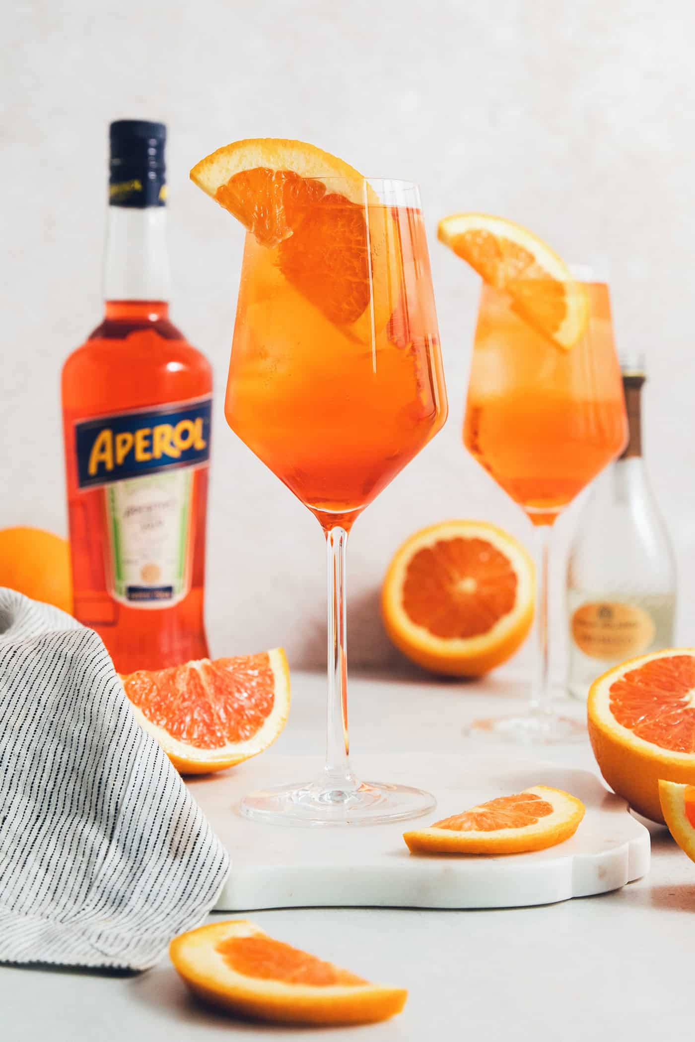 This classic Aperol spritz recipe is my take on an Italian aperitivo and makes a refreshing cocktail out of just four ingredients. Glasses of Aperol spritz are surrounded with orange wedges next to a bottle of Aperol.