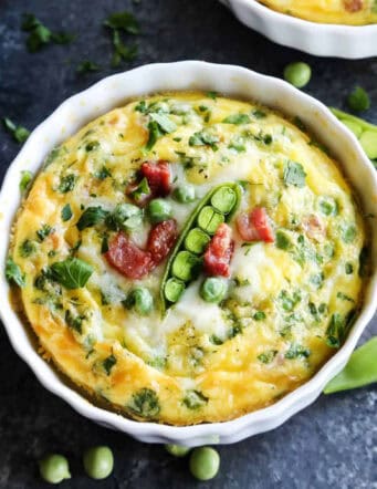A ramekin of baked eggs is topped with peas.