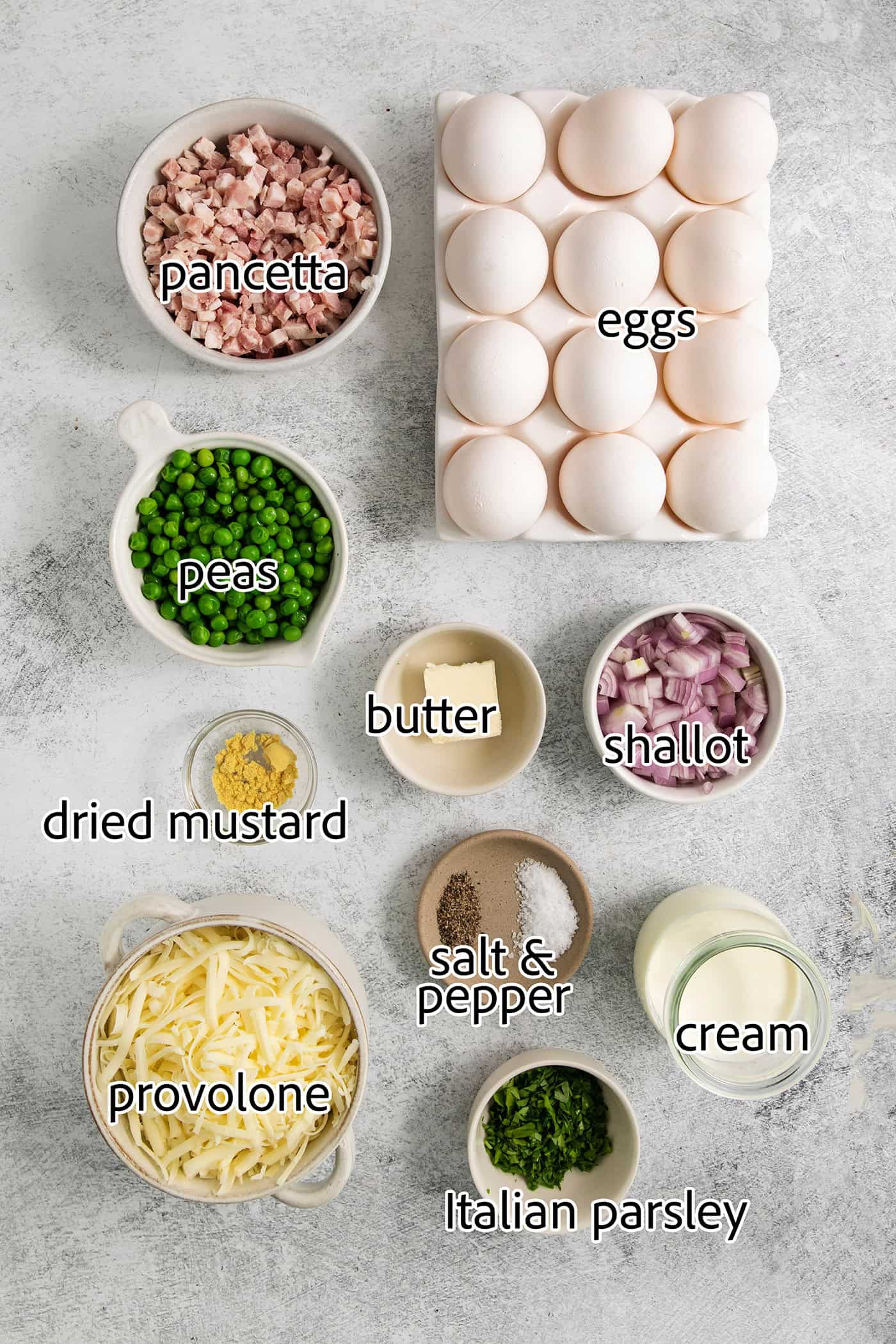 Soft and savory Baked Eggs are a welcome addition to the brunch table. Loaded with salty pancetta, melted provolone, and peas. Ingredients for baked eggs are shown portioned and labelled: eggs, butter, shallot, dried mustard, pancetta, peas, cream, provolone, salt and pepper, parsley.