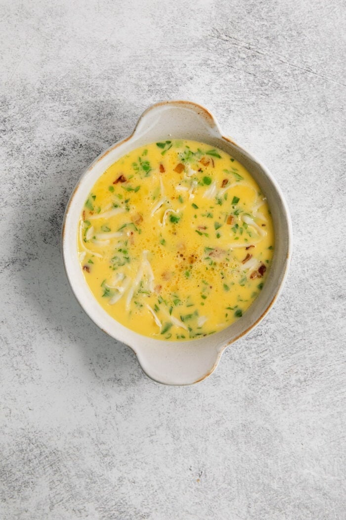 Soft and savory Baked Eggs are a welcome addition to the brunch table. Loaded with salty pancetta, melted provolone, and peas. The egg mixture in a ramekin.