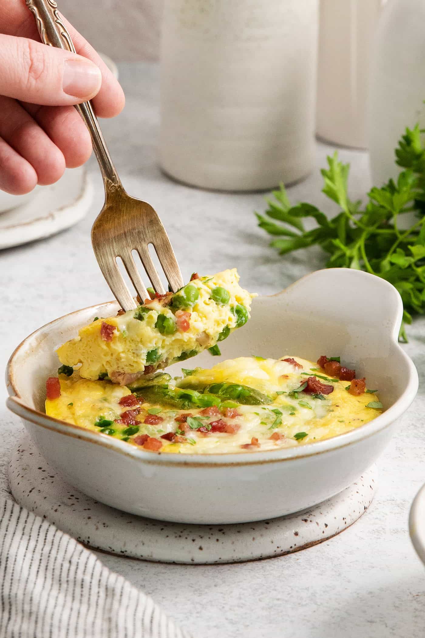 Soft and savory Baked Eggs are a welcome addition to the brunch table. Loaded with salty pancetta, melted provolone, and peas. A fork picks up a piece of a ramekin of baked eggs.