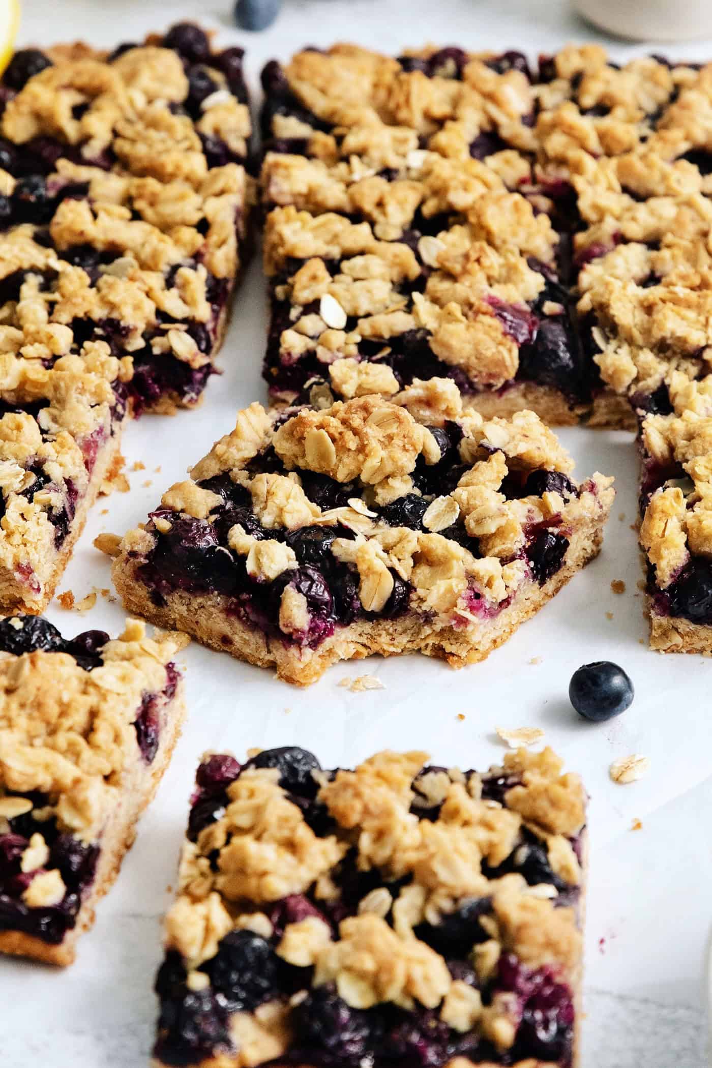 A batch of blueberry crumble bars, the one in the middle has a bite taken out.