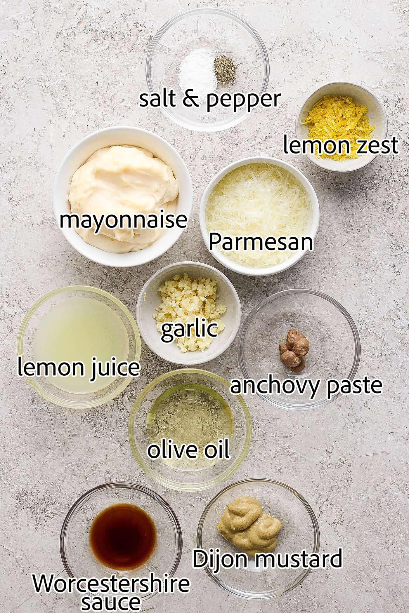 This gorgeously rich and creamy homemade Caesar Dressing recipe is perfect for making a classic Caesar salad. Takes minutes to make. Ingredients for caesar dressing are shown portioned out and labelled: lemon zest and juice, mayonnaise, parmesan cheese, anchovy paste, salt and pepper, Worcestershire sauce, mustard, olive oil.