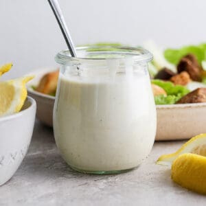 a small jar of Caesar dressing and a salad behind it