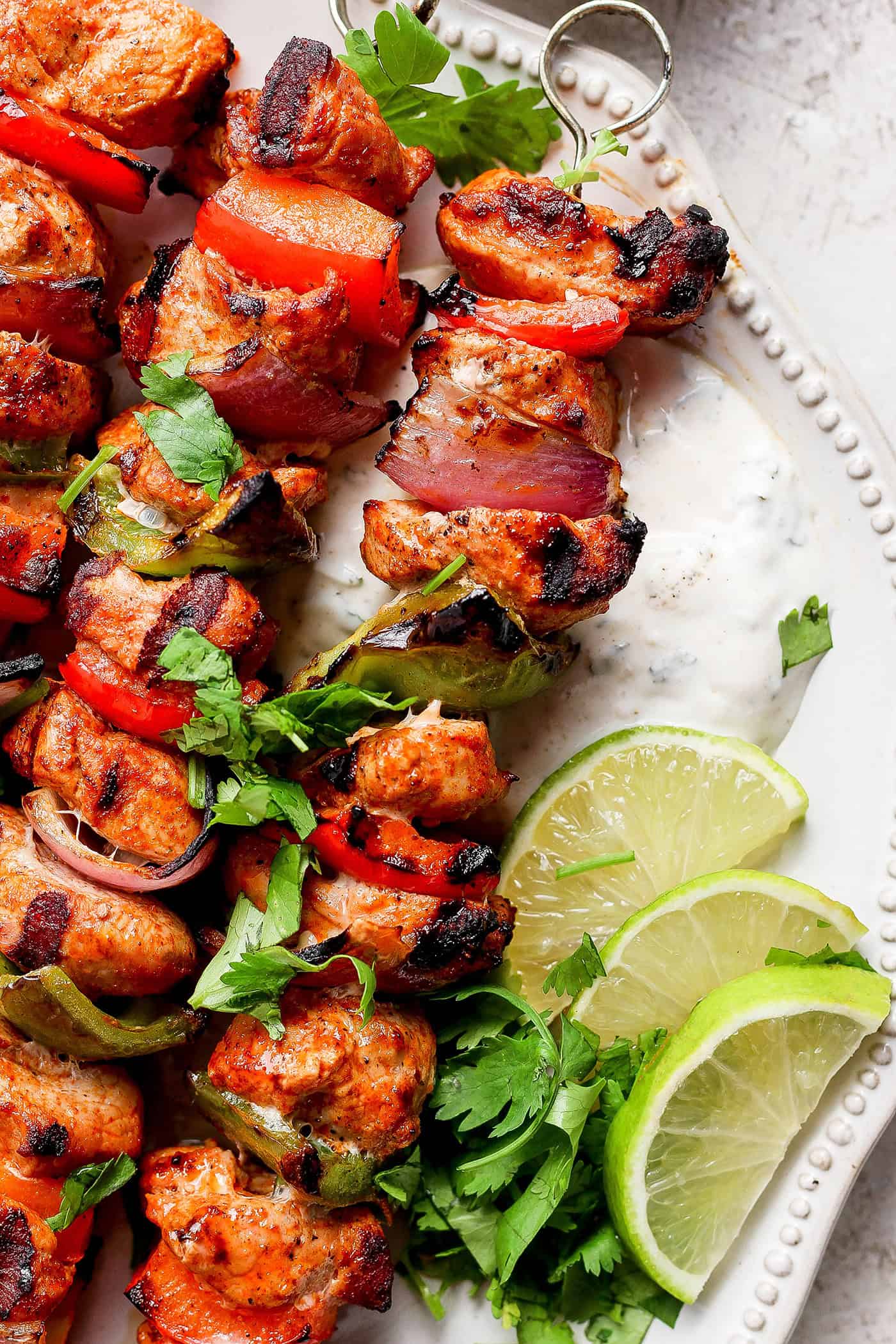 Grilled charmoula pork kabobs on a plate with lime wedges.