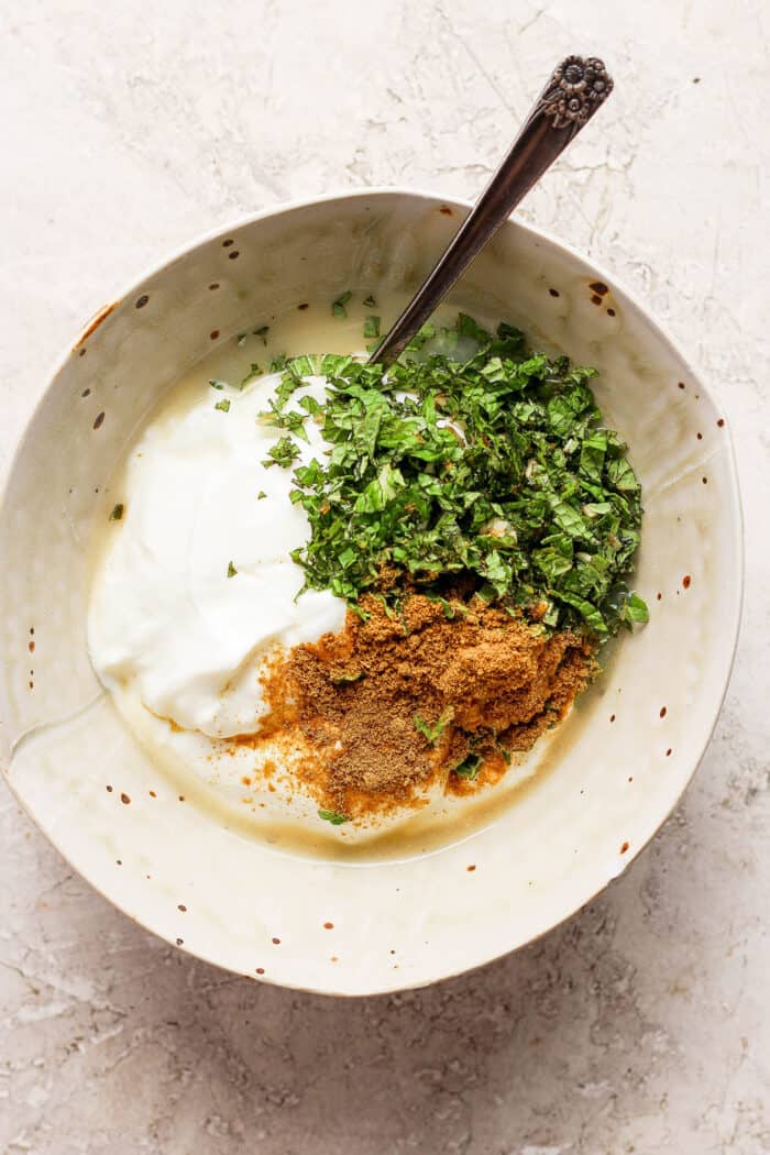 Greek yogurt, mint, and spices are placed in a bowl.