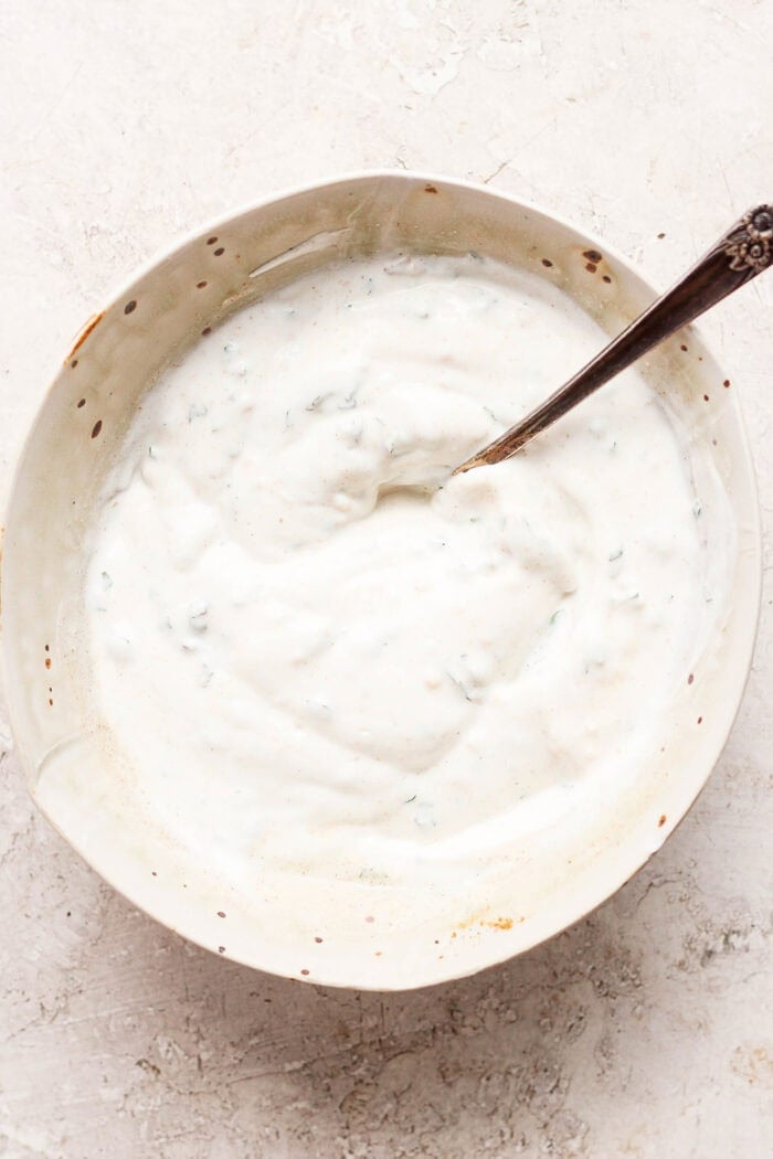 A spoon stirs the yogurt and mint sauce.
