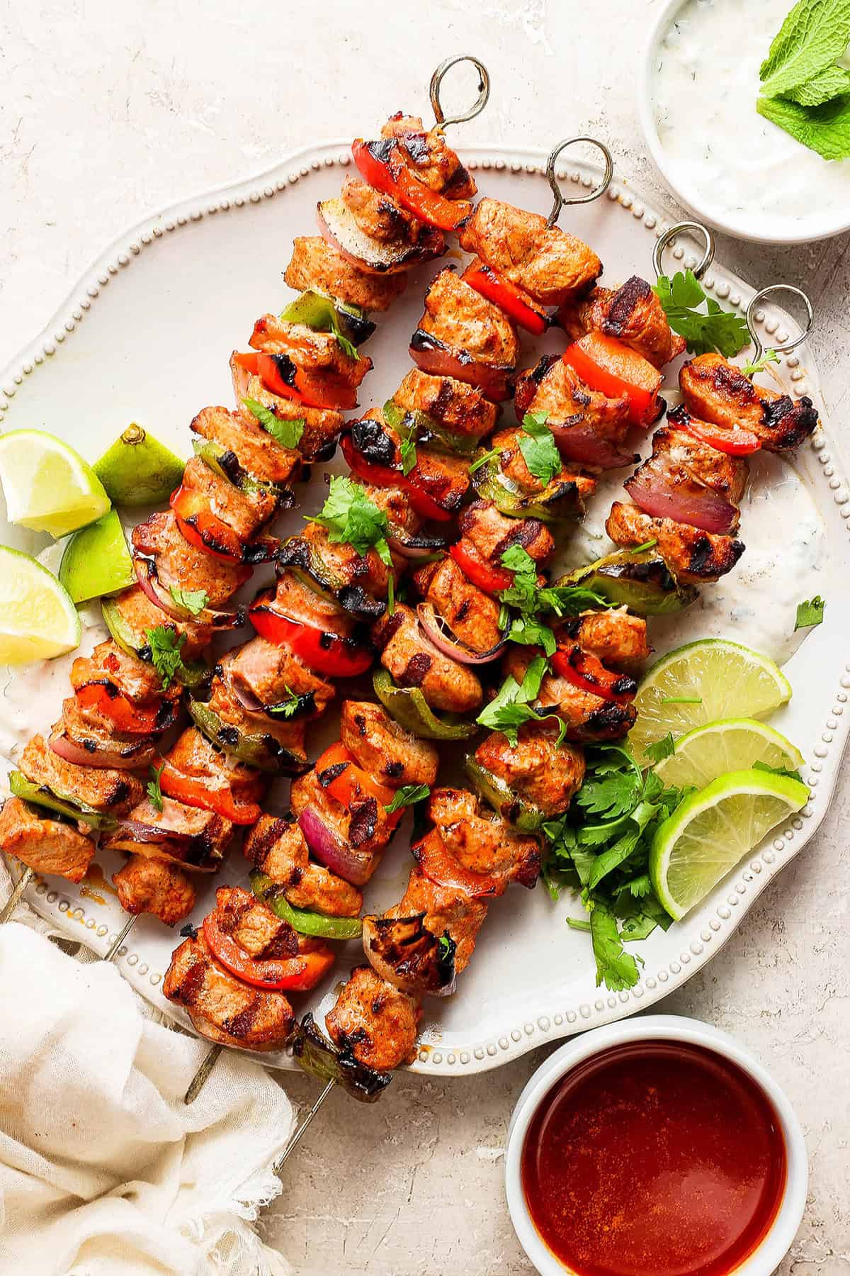Four grilled charmoula pork kabobs on a plate with lime wedges.
