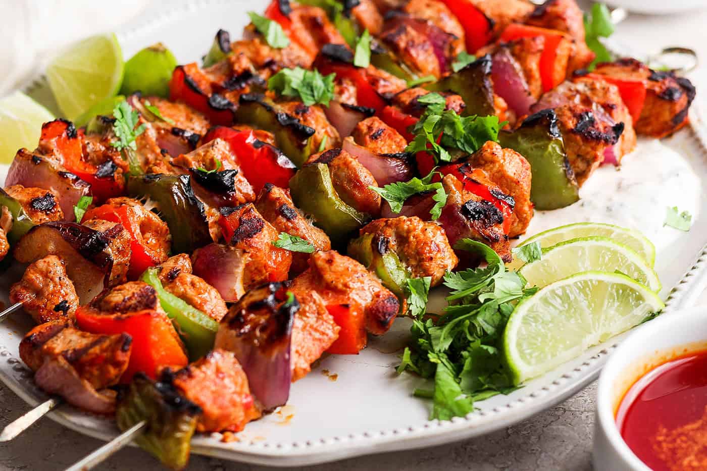 Four grilled charmoula pork kabobs on a plate with lime wedges.