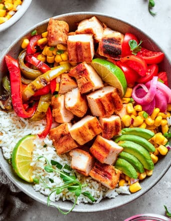 overhead photo of a fajita bowl with rice, chicken, corn salsa, pickled red onions, peppers, and avocado