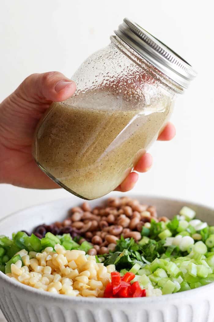 A hand shakes the jar to combine the dressing.