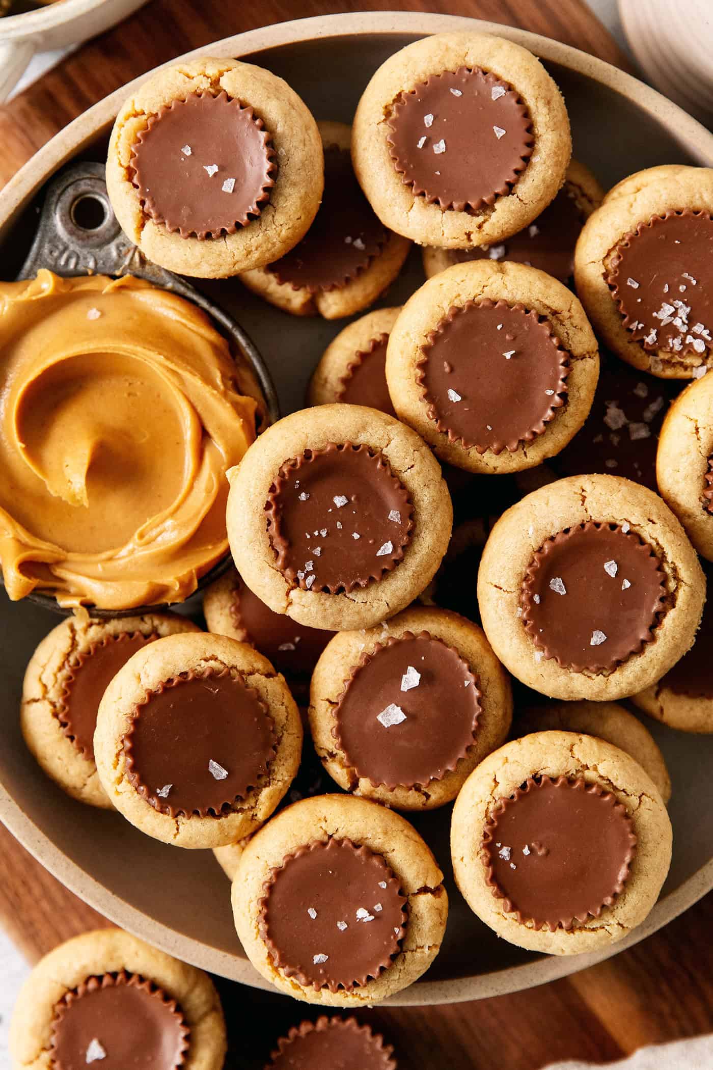 These Peanut Butter Cup Cookies feature soft and chewy peanut butter cookies stuffed with a gooey, chocolatey Reese's cup. Peanut butter cup cookies with a dish of creamy peanut butter next to them are served in a bowl.