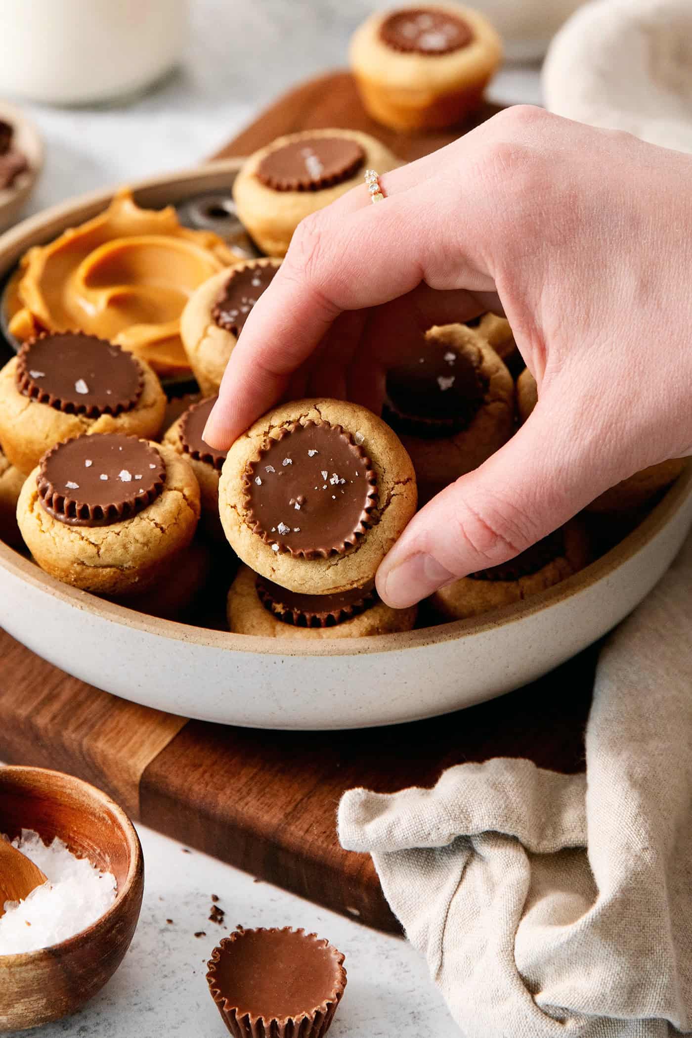 These Peanut Butter Cup Cookies feature soft and chewy peanut butter cookies stuffed with a gooey, chocolatey Reese's cup. A hand lifts out a peanut butter cup cookie from a bowl.