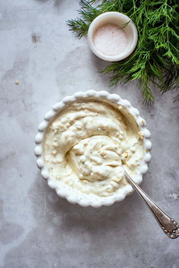 Creamy, crunchy, and puckery dill Pickle Pizza is a fun twist on classic pizza with white sauce, fresh and shredded mozzarella, dill, and plenty of pickles. A spoon mixes the white sauce ingredients in a bowl.