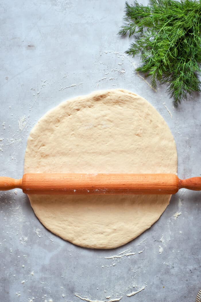 A rolling pin rolls out the pizza dough into a round.