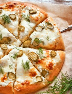 A baked pickle pizza with white sauce is ready to eat.