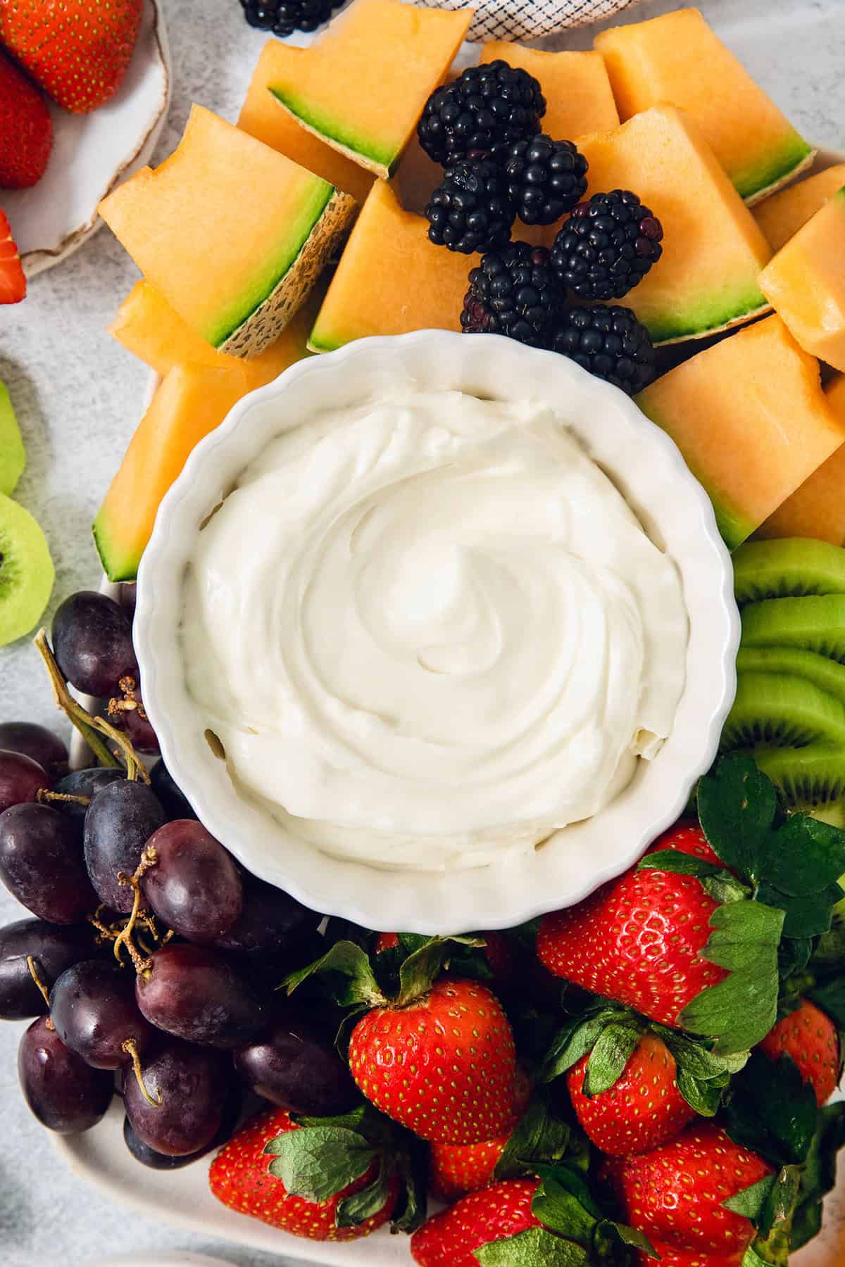 A bowl of fruit dip is served surrounded by fresh fruit.