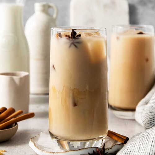 A tall glass of iced chai latte with another in the background.