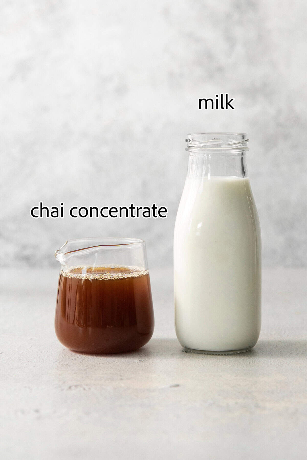 This easy Iced Chai Latte recipe is the perfect refreshing drink, featuring crisp black tea, warm spices, and a hint of brown sugar. Ingredients needed for a chai latte are shown labeled in glass containers: chai concentrate, milk.