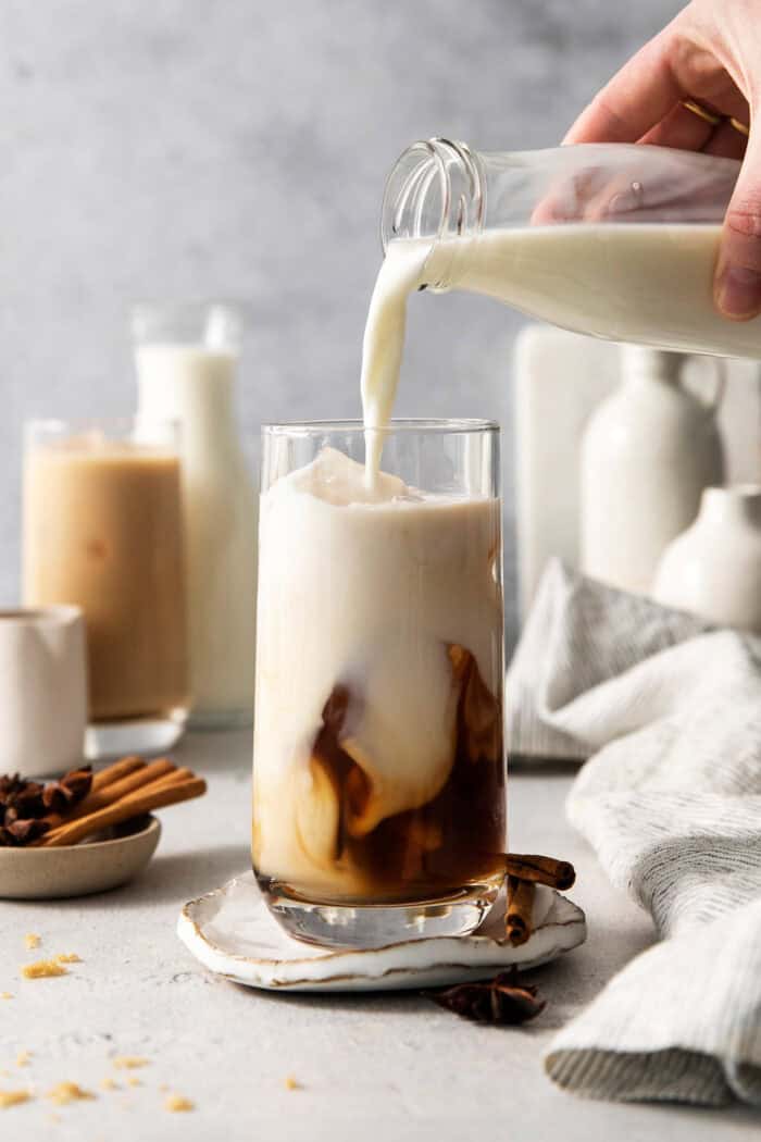 This easy Iced Chai Latte recipe is the perfect refreshing drink, featuring crisp black tea, warm spices, and a hint of brown sugar. Milk is poured into the glass with the chai and ice.