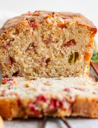 A loaf of rhubarb bread cut to show a slice and the pink spots of rhubarb.
