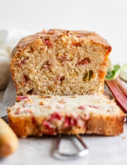 A loaf of rhubarb bread cut to show a slice and the pink spots of rhubarb.