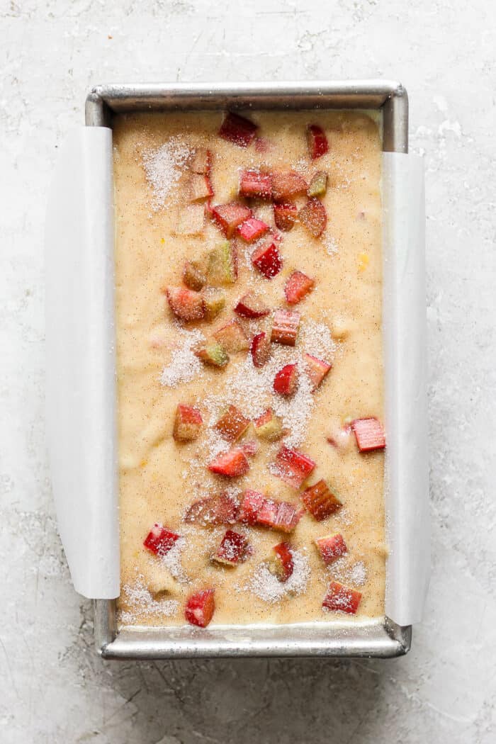 This Rhubarb Bread is gorgeously moist and tender, warmly spiced with cinnamon and spiked with orange zest. Bits of rhubarb top a rhubarb bread batter in a pan.