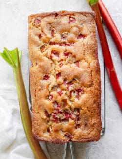 A baked rhubarb bread loaf with stalks of rhubarb next to it.