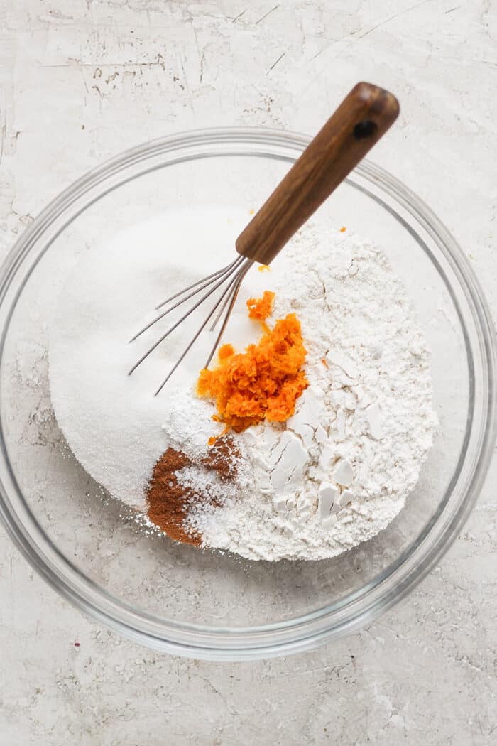 dry ingredients for muffin batter in a clear mixing bowl, with a whisk