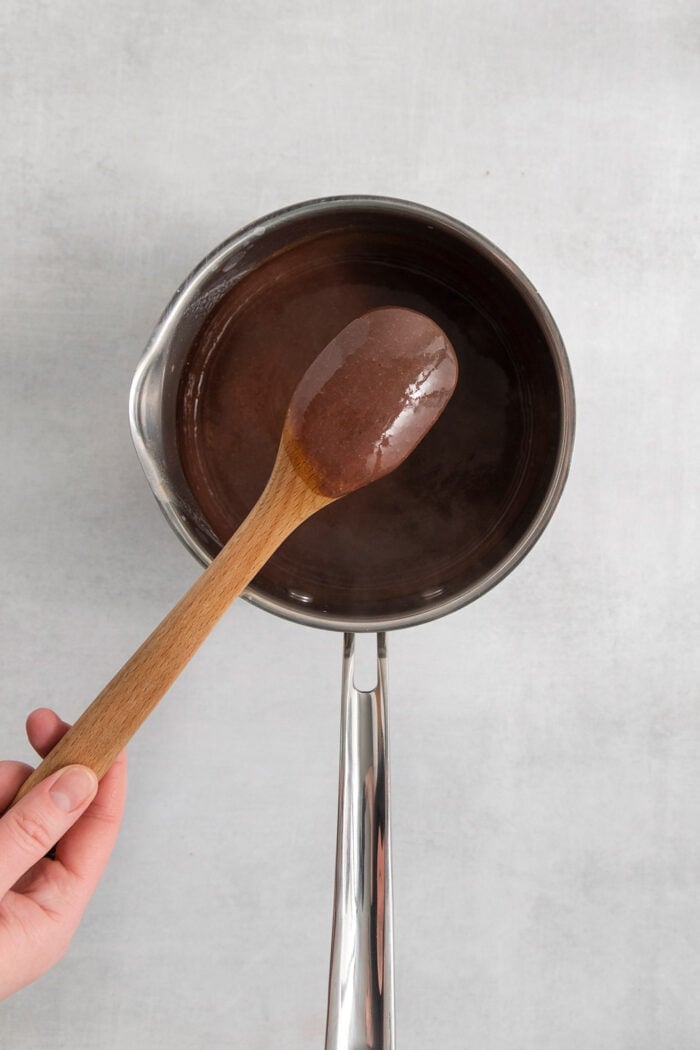Rocky Road Ice Cream stars a creamy chocolate custard base that's loaded with almonds, marshmallows, and even more chocolate! A spoon lifts out a little of the ice cream custard from the pot to show its thickness.