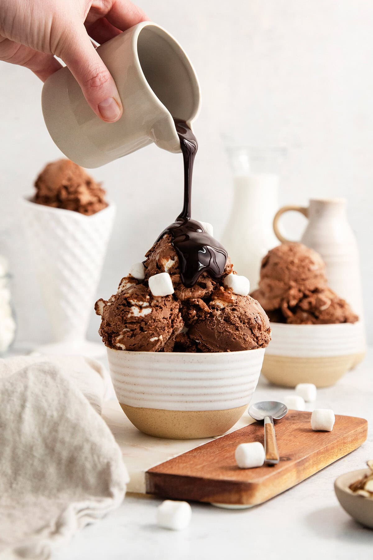 Chocolate sauce is poured over scoops of rocky road ice cream in a bowl.