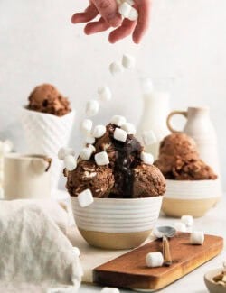 A hand drops a ferw mini marshmallows over a bowl of rocky road ice cream.