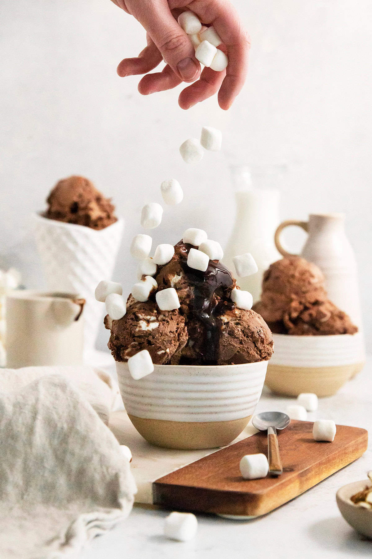 A hand drops a ferw mini marshmallows over a bowl of rocky road ice cream.