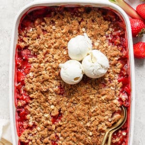 strawberry rhubarb crisp in a white rectangular baking dish, with scoops of ice cream on top