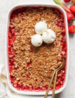 overhead photo of strawberry rhubarb crisp in a white rectangular baking dish, with scoops of ice cream on top