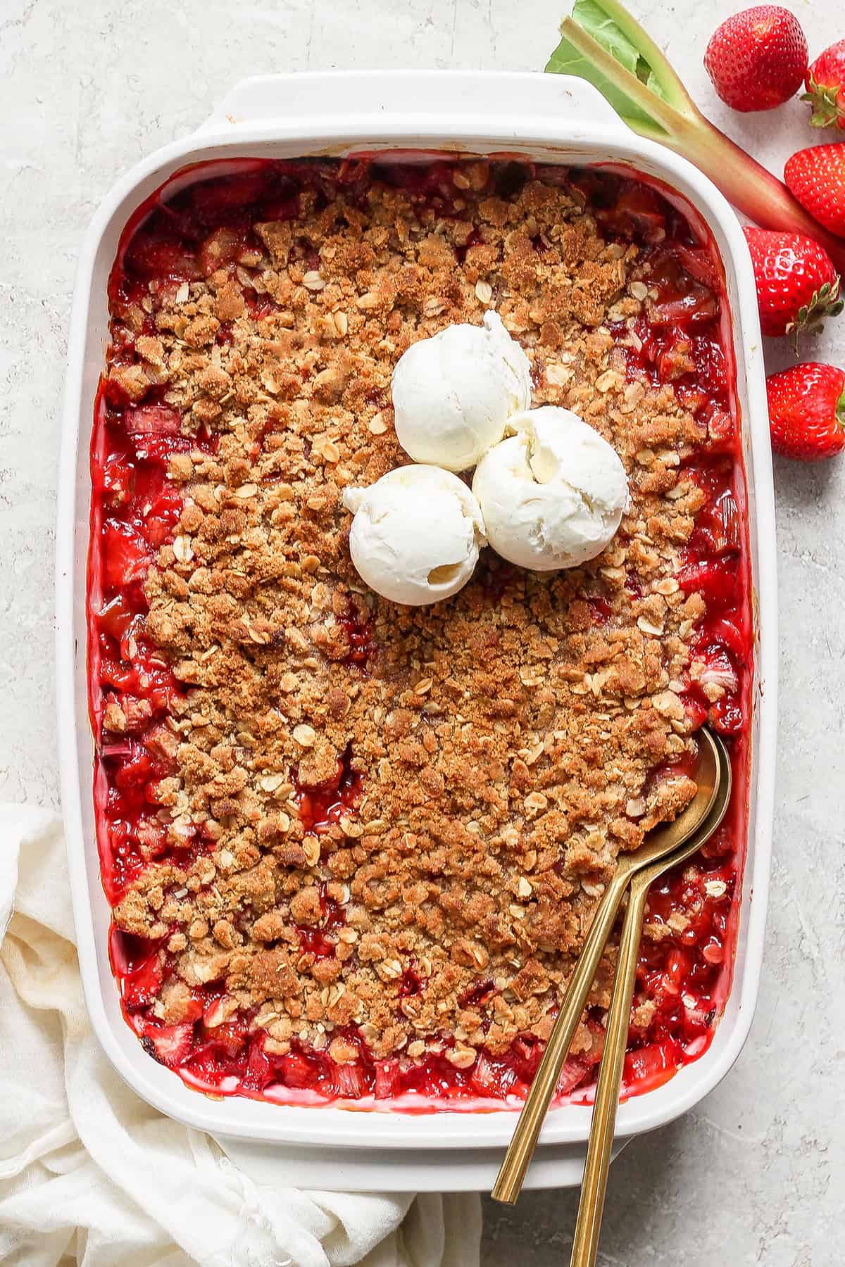 overhead photo of strawberry rhubarb crisp in a white rectangular baking dish, with scoops of ice cream on top
