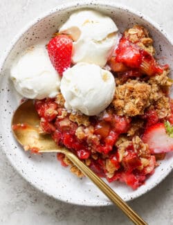 individual bowl of strawberry rhubarb crisp, with scoops of vanilla ice cream