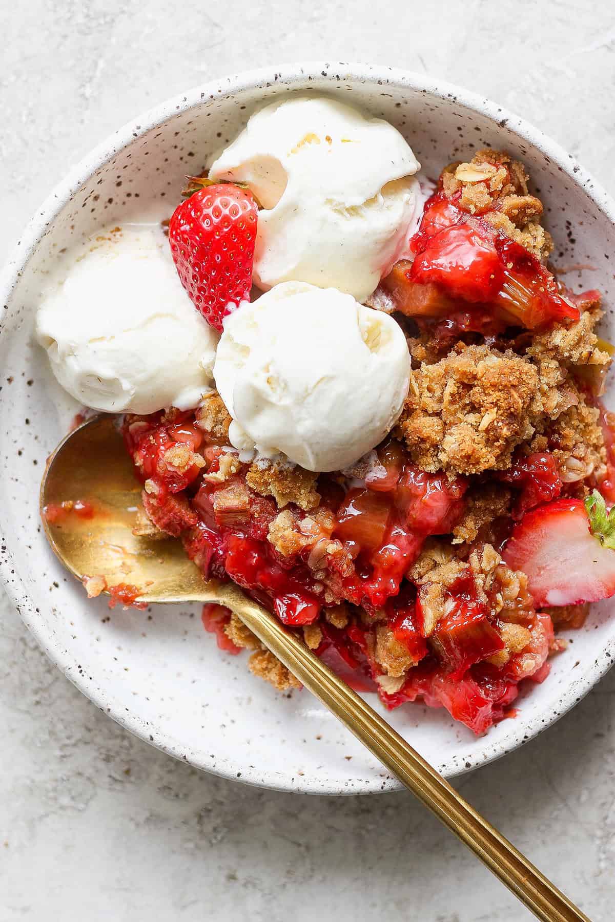 individual bowl of strawberry rhubarb crisp, with scoops of vanilla ice cream