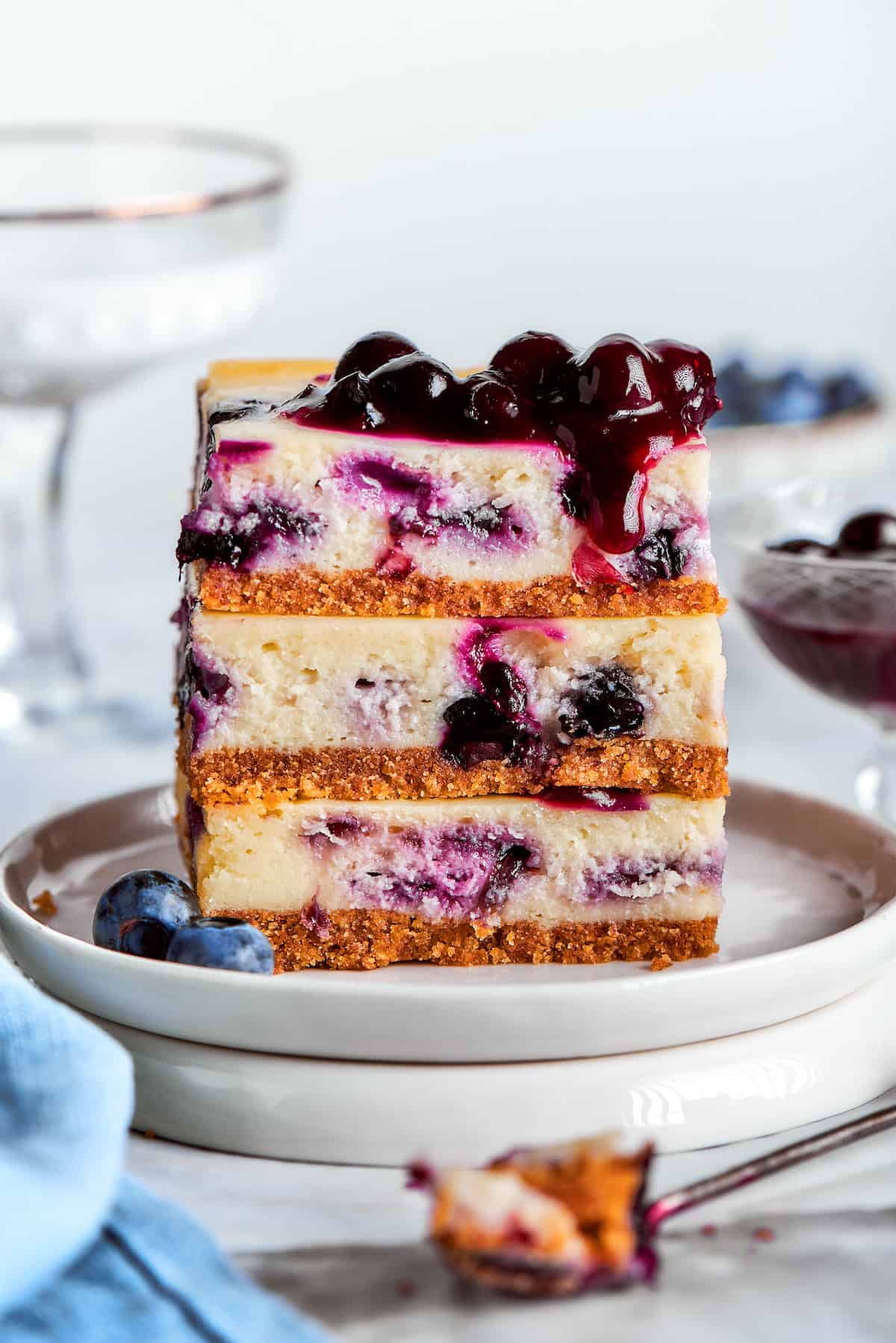 a stack of 3 blueberry cheesecake bars on a white plate