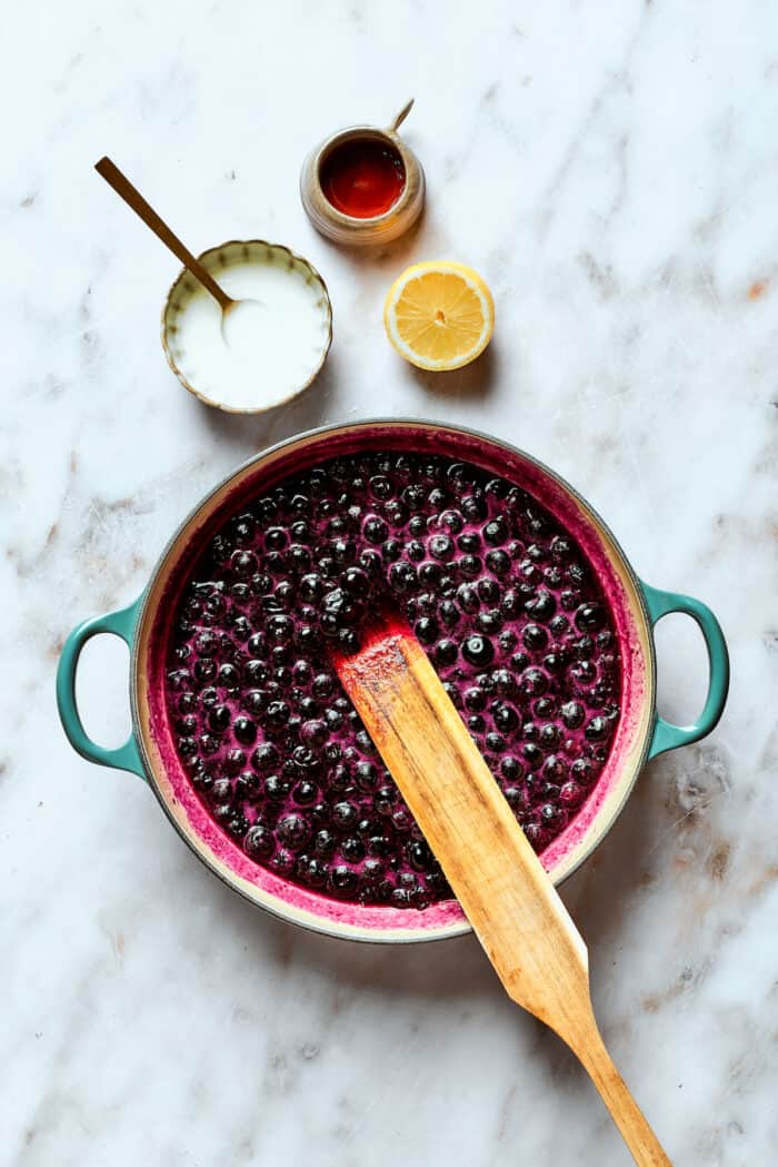 A wooden spoon stirs the blueberries and sugar.