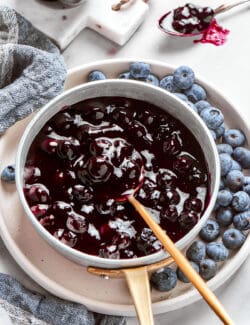 A pot of blueberry sauce with a spoon on a plate.