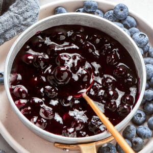 a spoon in a pan of fresh blueberry sauce, plus fresh blueberries