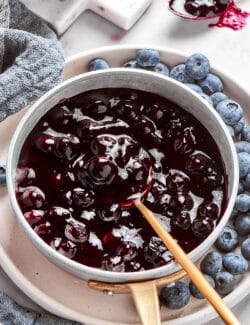 a spoon in a pan of fresh blueberry sauce, plus fresh blueberries