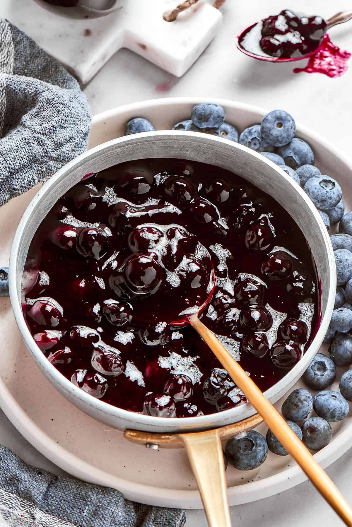 a spoon in a pan of fresh blueberry sauce, plus fresh blueberries