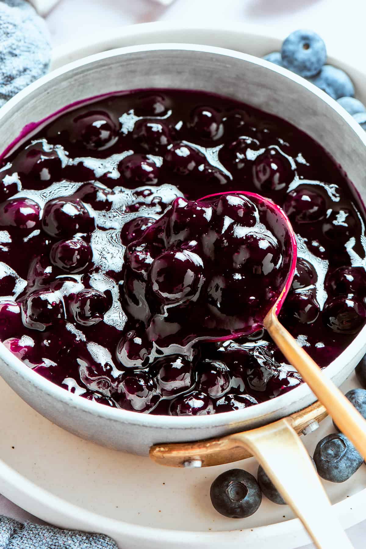 A gold spoon stirs a pot of blueberry sauce.