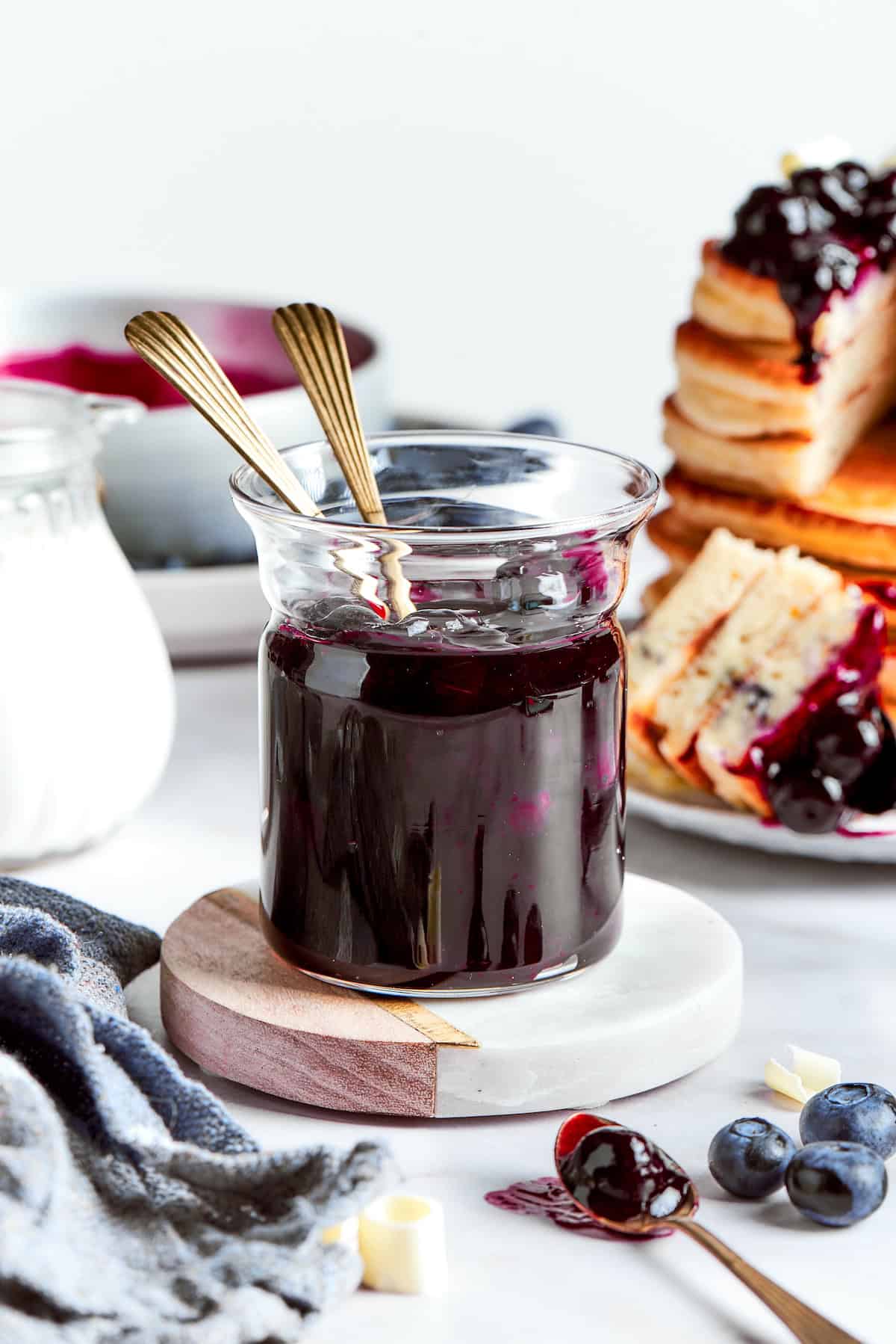 A jar of blueberry sauce with pancakes in the background.