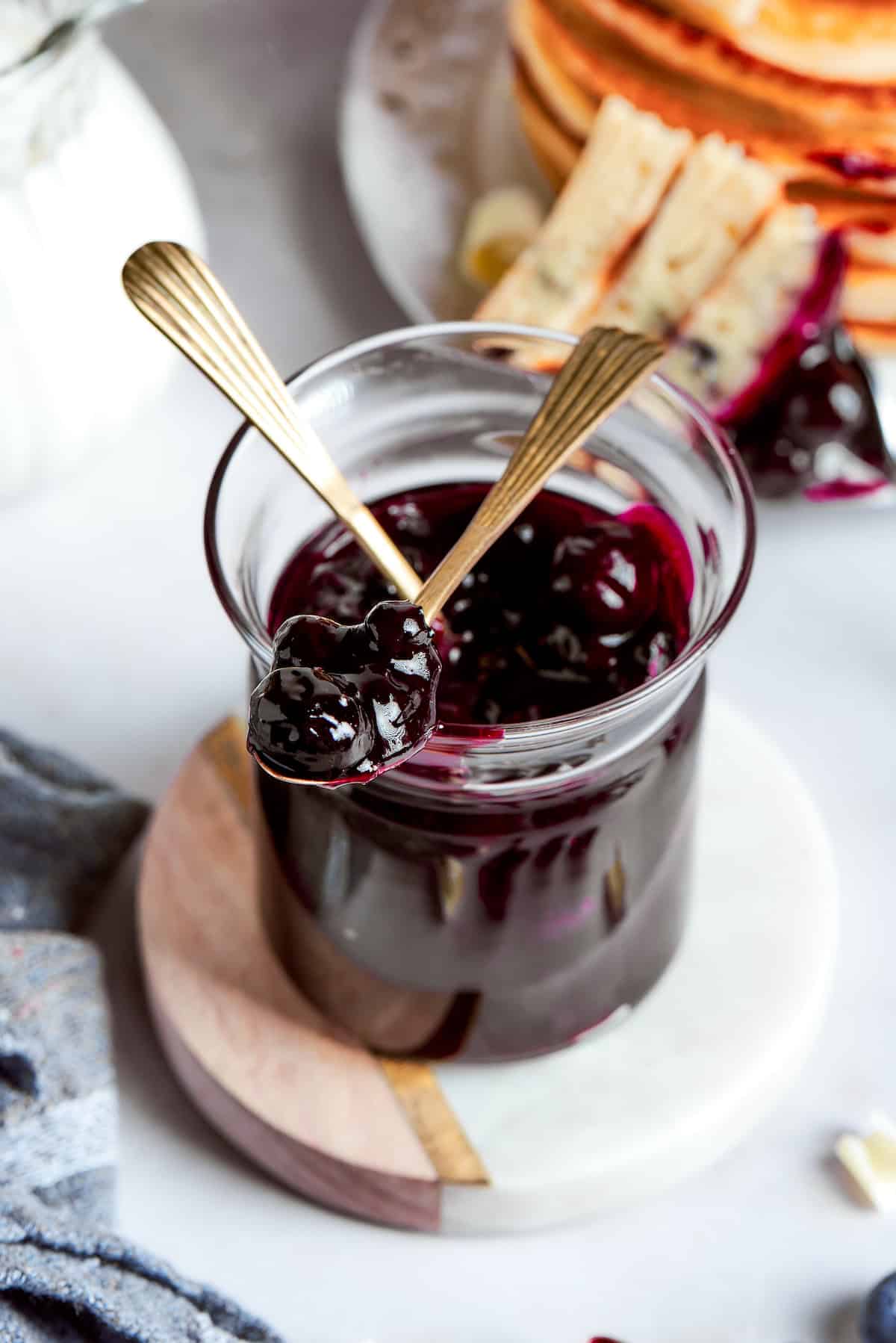 Two spoons are placed in a glass container of blueberry sauce.