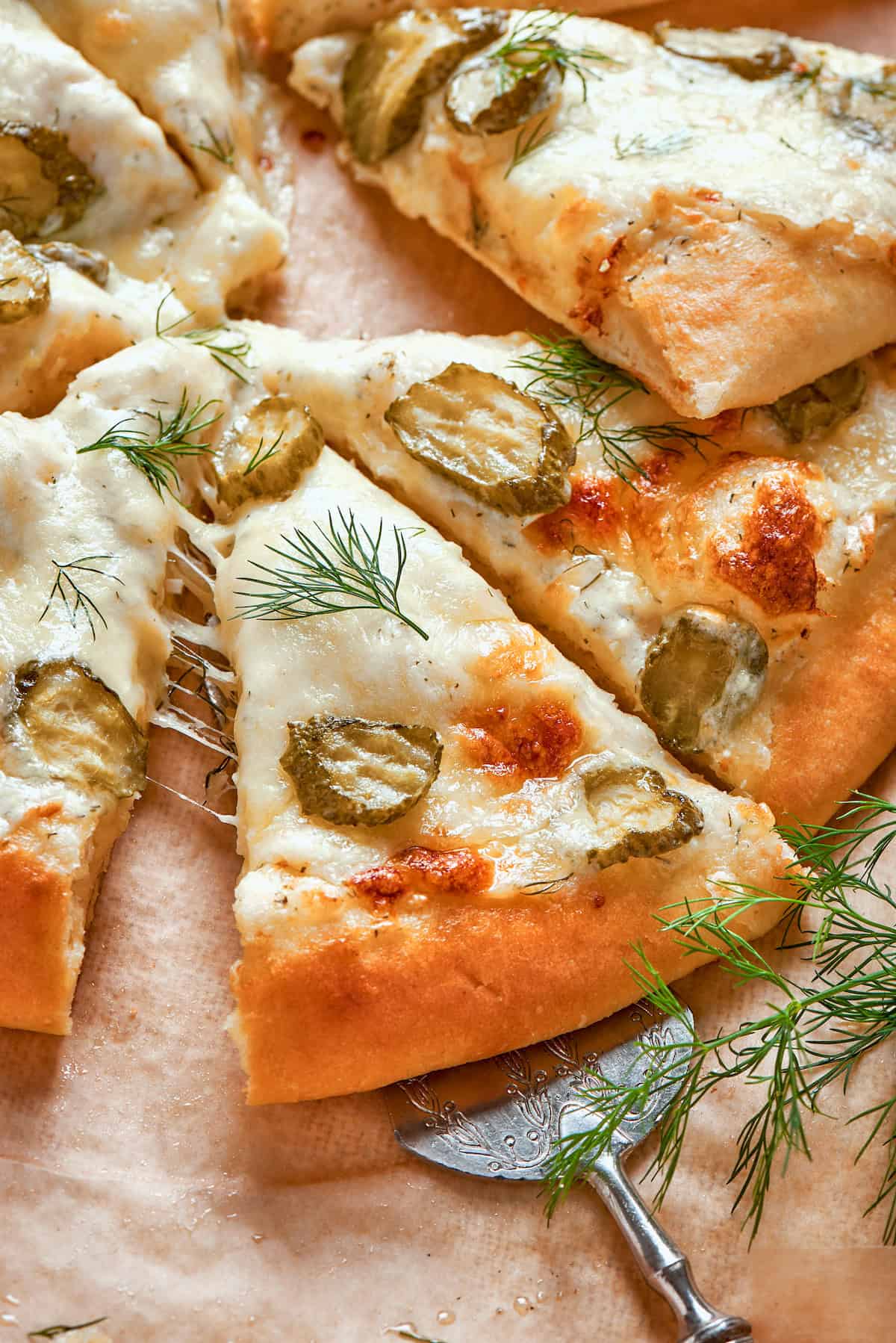 a spatula taking a piece of pickle pizza away from a whole pizza