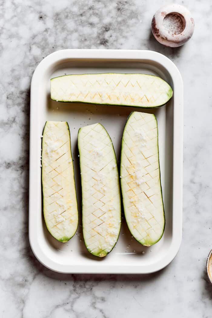 The zucchini are halved and placed in a baking dish.