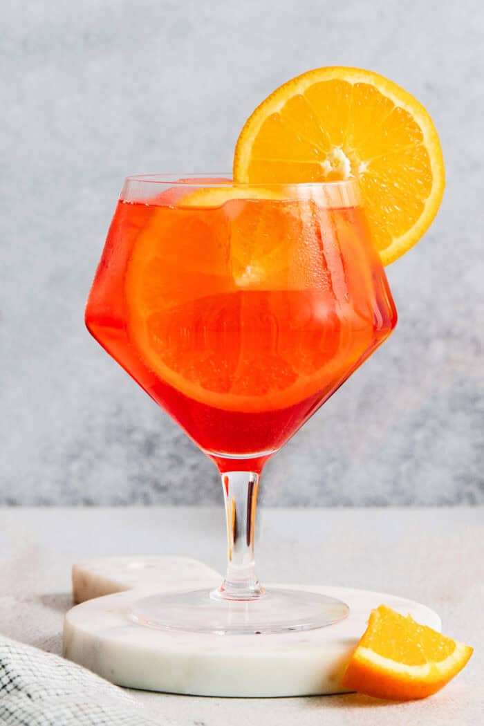 This refreshing, ruby-red Campari Spritz is a beautifully simple drink made with just 3 ingredients including campari and Prosecco. a glass of Campari spritz with an orange wheel garnish